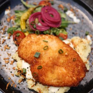 A crispy pork chop on mashed potatoes with fresh vegetables on a plate.