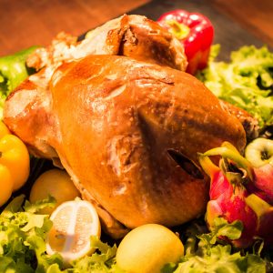 Close-up of a roasted chicken surrounded by fresh bell peppers and lettuce, perfect for dinner.